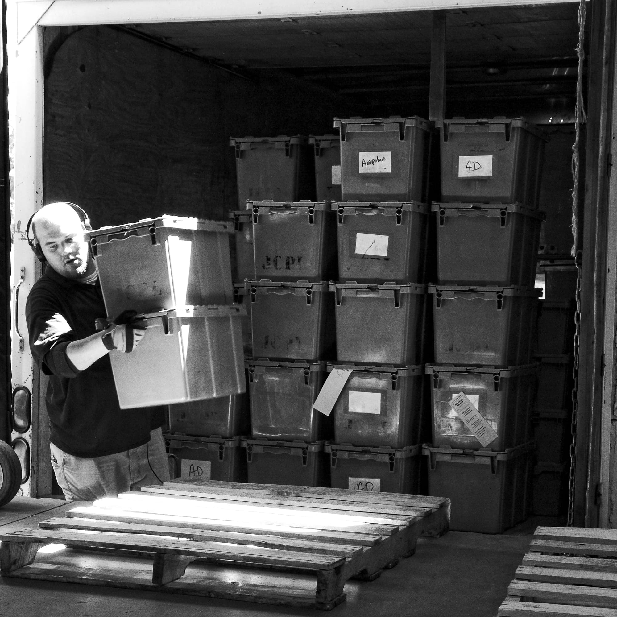 A courier lifts library bins inside a delivery truck stacked with labeled totes